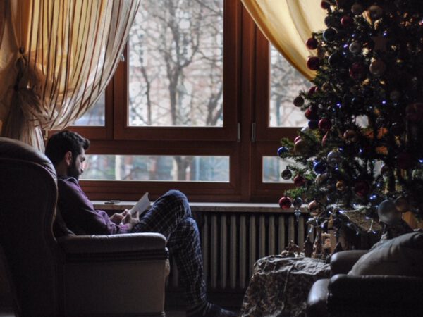 Single-Tipps für die Weihnachtsfeiertage - Ein Mann sitzt alleine am Fenster neben einem Weihnachtsbaum.